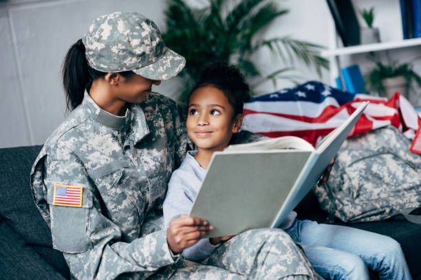 african american daughter and mother in military uniform reading book together at home